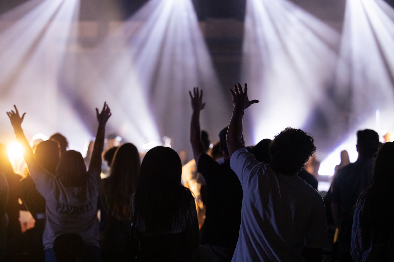 A worship crowd in silhouette, hands raised toward the stage lights